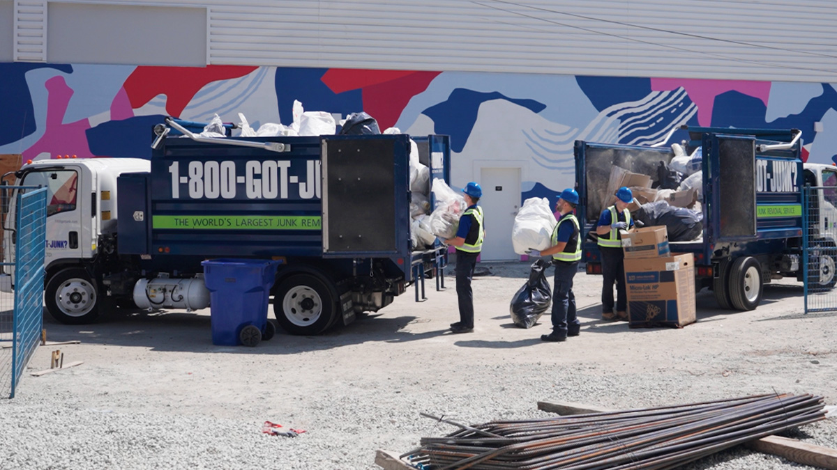 1-800-GOT-JUNK? truck team members loading waste bags filled with construction debris onto the truck bed.”