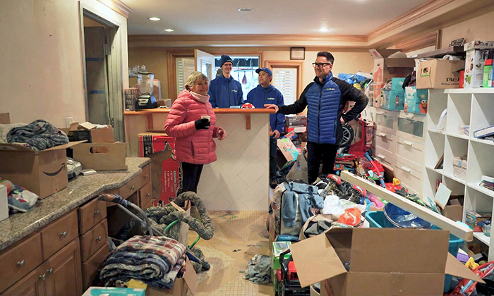 Une femme se tient devant sa maison désencombrée avec le fondateur de 1-800-GOT-JUNK?, Brian Scudamore et deux équipiers, en observant la collection de ses objets encombrants. 